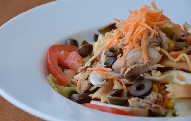 Image of farfalle pasta salad with tuna, shredded carrots, black olives, and tomato.