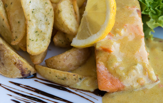 Image of grilled salmon with special Spanish sauce and a side of potato wedges from Clay's platters menu