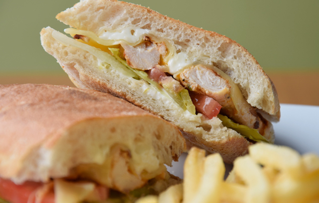 Photo of grilled chicken sandwich in Ciabatta bread with melted cheese, tomato, lettuce and a side of french fries.