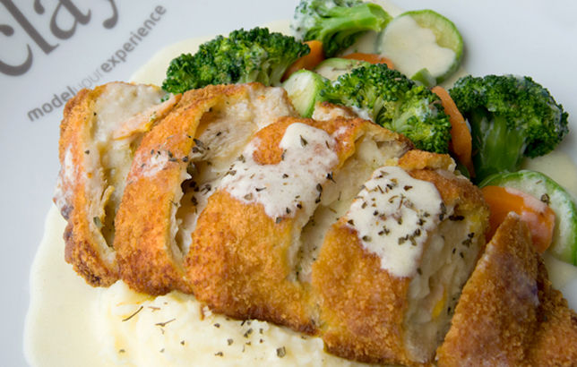Image of breaded chicken stuffed with cheese, parsley, and turkey, served over mashed potatoes with a side of seasoned vegetables.