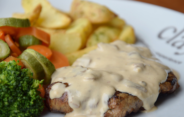Photo of high quality medium-well steak filet with mushroom sauce, seasoned vegetables, and potato wedges from Clay's platters menu